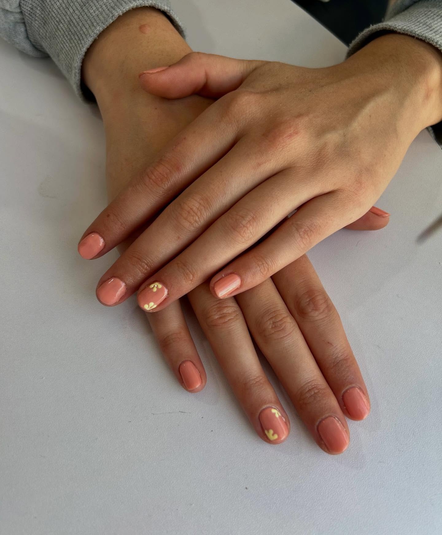 Manicura en tono coral con diseño floral minimalista, realizada en Peluquería y belleza unisex en Yeste